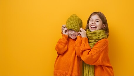 winter portrait of happy children wearing knitted hat, snood and sweaters. girls having fun, playing and laughing on yellow background. fashion concept.