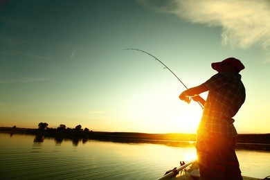 young man fishing on a lake from the boat at sunset