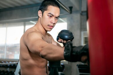 athletes asian man boxer training on a punching bag at fitness gym.