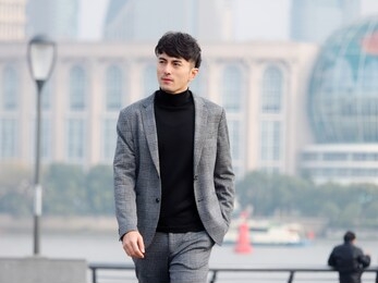 confident and handsome chinese young business man in casual suit walking outdoor with hand in his pocket against shanghai bund background, chinese businessman lifestyle concept.