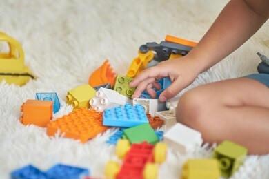 happy asian boy playing with colorful construction plastic blocks on white bed at home.