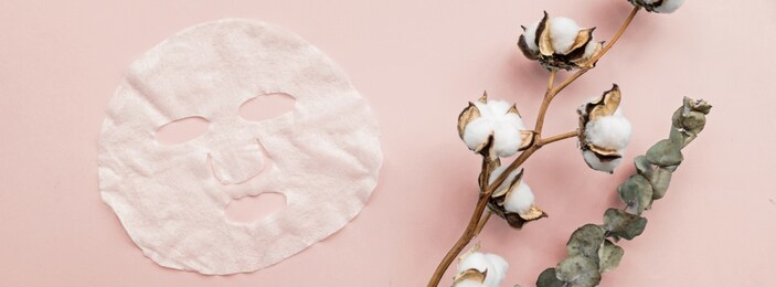 sheet facial mask, eucalyptus and cotton flower on pastel pink paper background. banner for web design. skin care, dermatology, beauty concept. top view, flat lay, mockup, overhead, copy space