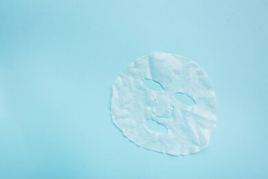 sheet facial mask on pastel blue paper background. skin care, dermatology, beauty concept. top view, flat lay, mockup, overhead, copy space, template