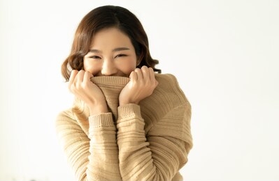 portrait of inspired caucasian asian lady covers her mouth with a collar of beige sweaters and smilling at camera. concept woman lifestyle , cosmetics, beauty salon and winter. autumn, winter season.
