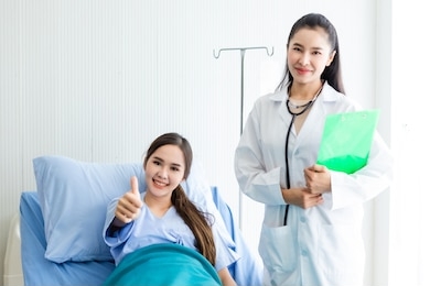 asian young female patient on bed showing thumbs up with smiley face very good symptom to asian young female doctor in hospital background.