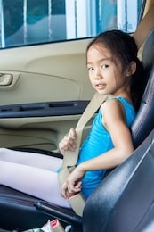 an asian girl wears a seat belt by herself in a car with a left-hand threaded steering wheel.
