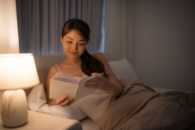leisure and people concept - young woman reading book in bed at night home