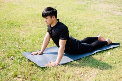 man in black cloth do yoga on yoga mat at the field in the strong sunshine.