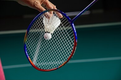 hands of badminton player holding shuttlecock and racket ready to serve with green badminton court background 