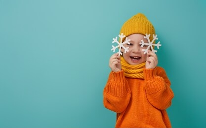 winter portrait of happy child wearing knitted hat, snood and sweater. girl having fun, playing and laughing on teal background. fashion concept.                               