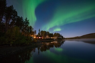 northern lights (aurora borealis) reflected over lake in kiruna, sweden.