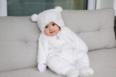 adorable little baby wearing white teddy bear costume sitting on sofa he is about 5 months old. happy mixed race asian-german boy