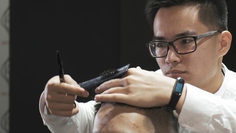 close-up asian hairdresser with glasses combing and cutting hair to client in salon. creates a modern hairstyle