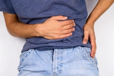 young man in jeans and t-shirt holds hands to his stomach and back, hernia or sports back injury concept 