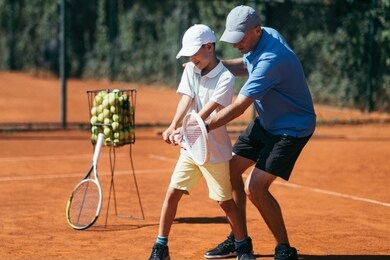 boy training with tennis instructor on a clay court