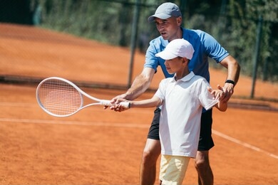 boy training with tennis instructor on a clay court