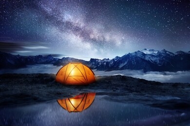 camping adventure in the mountains. a tent pitched up and glowing under the milky way. photo composite.