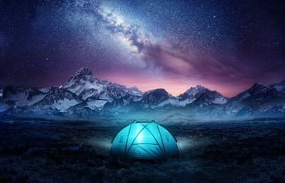 camping in the mountains under the stars. a tent pitched up and glowing under the milky way. photo composite.