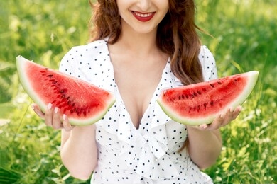 beautiful woman holds two pieces of watermelon. nice girl is holding two slices of watermelon on green background of summer sunny day.