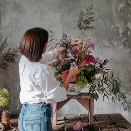 female professional florist prepares the arrangement of wild flowers. flower shop. background concrete gray wall. concept inspiration, floral, greetings, spring, ornament flowers.