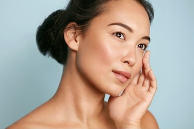 skin care. woman with beauty face and healthy facial skin portrait. beautiful asian girl model with natural makeup touching glowing hydrated skin on blue background closeup. high quality image