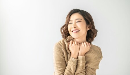 portrait of young beautiful asian woman relax in bedroom. smile happy asian girl hands cover face wear winter cloth. beauty treatment perfect clear skin japanese woman makeup winter concept banner