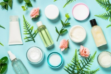 beauty background with natural cosmetic, green leaves and flowers. flat lay image on blue.