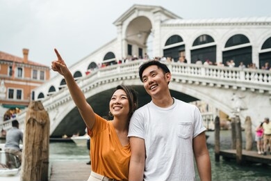 portrait of a young and beautiful asian couple visiting the city of venice, italy - millennials on their honeymoon, behind them the rialto bridge