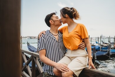 portrait of a beautiful young asian couple kissing on vacation in venice, italy, behind them the lagoon and gondolas - millennial on their honeymoon -