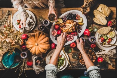thanksgiving party table setting. flat-lay of whole roasted chicken, vegetables, fig pie, fruit, pumpkin, candles, tableware, eating people and tiger cat over rustic wooden table background, top view