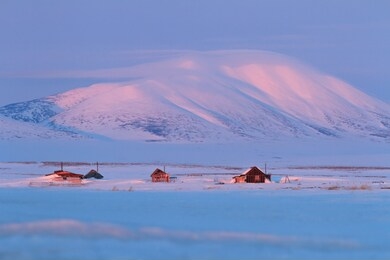 winter landscape with snow-covered houses and a mountain. soft morning light. abandoned cottages in the tundra. cold may in the arctic. chukotka, siberia, far east of russia.