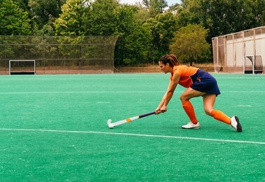 female hockey player attacking and hitting on a grass field.