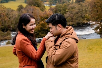 happy attractive asian couple fall in love, man hold woman hand kiss with diamond ring after make proposal to get married engagement, young newlywed holiday, vacation honeymoon in autumn season