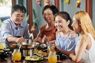 happy preteen girl eating tasty dinner with her family in restaurant when celebrating some event together