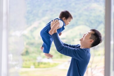 attractive young asian father is holding and playing together with his little baby boy at the balcony in the morning time, concept of love, relation and trust and happy moment in family lifestyle .