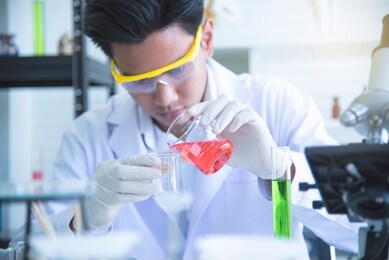 asian young  scientist is researching the experiment to pour chemicals for use in production. look at the test tubes in a science laboratory.