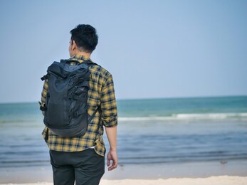 happy asian man wih backpack standing at the beach.