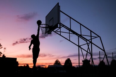 silhouette dunking man at sunset. basketball player scoring. young silhouetted man jumping high to the target basketball hoop achieves to score with a flying slam dunk at sunset.