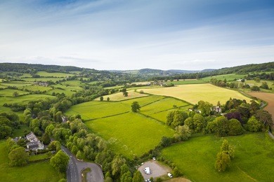 dramatic aerial view of idyllic rolling patchwork farmland with pretty wooded boundaries, lit in warm early evening sunshine in the heart of the cotswolds, england, uk.