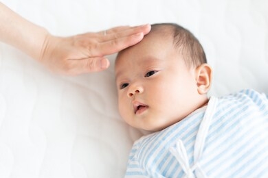 woman touching baby's forehead to take  temperature