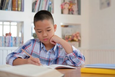 young little asian kid boy schoolboy writing drawing on notebook. child children doing homework. childhood education