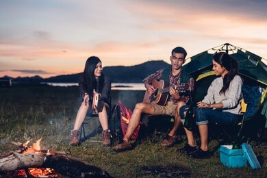 camping tent camp in nature happy young asian friends group people in night party bonfire and the man playing guitar together girlfriend in summer at nature forest, outdoor holidays summertime concept