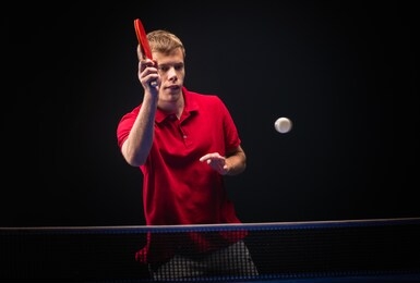 young man playing table tennis on black studio background.