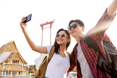 asian couple tourists taking selfie while traveling in bangkok thailand with giant swing and buddhist temple in background