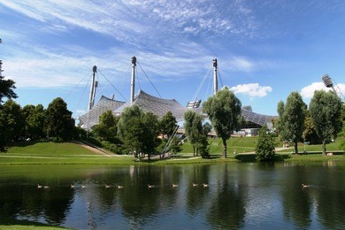 olympiastadion in munich, germany. a duck family passing by on a lake in front of it.