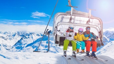 happy family on ski lift chair enjoying winter ski vacations in mountains  playing with snow and sun in high mountains. winter holidays.