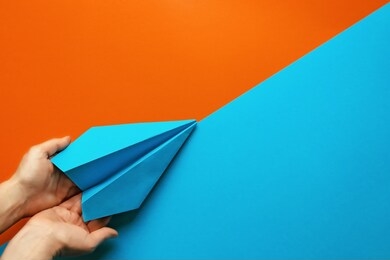 top view of woman hands supporting handmade blue paper plane on colorful geometric background. minimalism, support, startup and new beginning concept. 