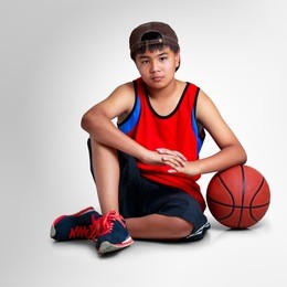 asian boy sitting with basketball on grey background with clipping path