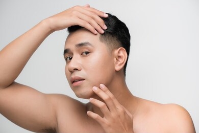 portrait of shirtless young handsome asian man checking his face for skin care and beauty concepts