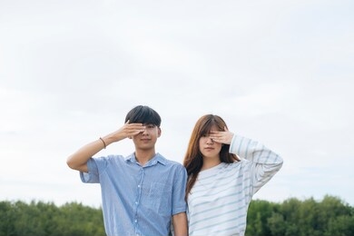 young asian couple covering their eye with hand looking at camera.